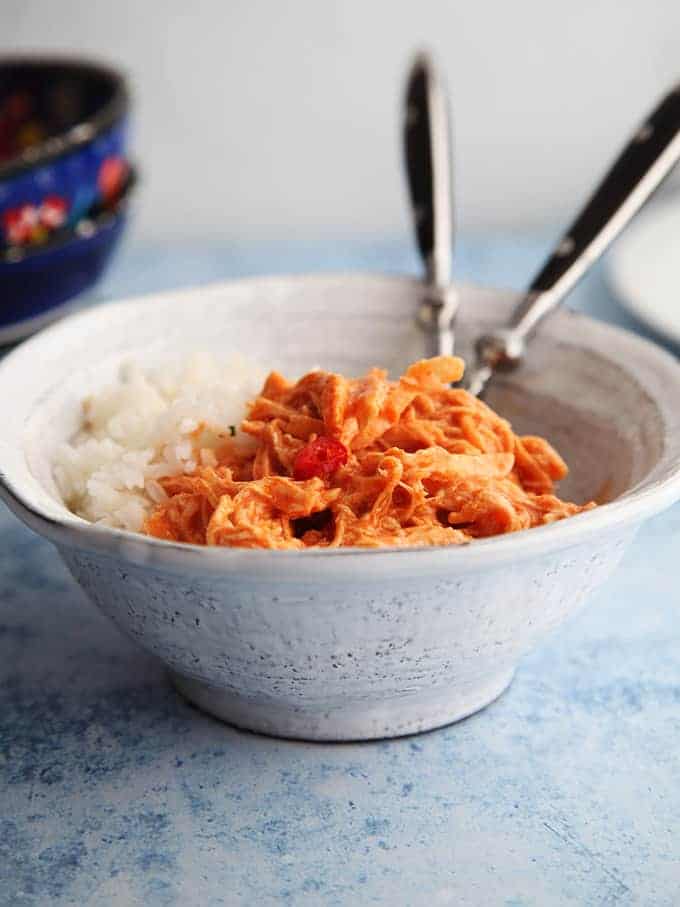 A bowl of buffalo chicken with rice on a white table