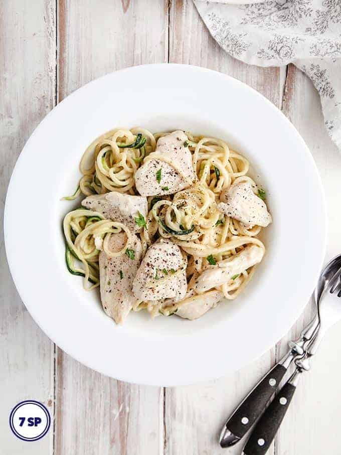 A white bowl of chicken Alfredo with zucchini noodles
