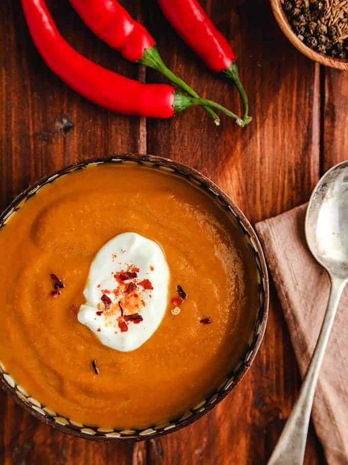 A bowl of curried pumpkin soup with some red chili on a wooden table