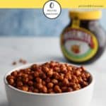 A white bowl of marmite chickpeas on a white table with a pot of marmite