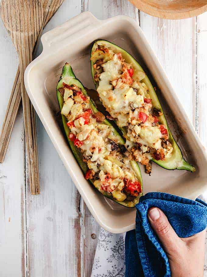 A dish of stuffed zucchini being placed on a white table