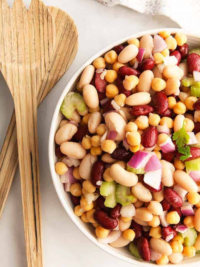 A white bowl full of three bean salad with wooden salad servers