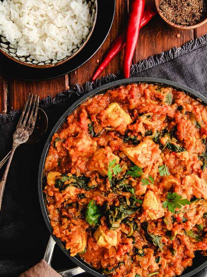 A skillet full of zero point curry with some chilies and a bowl of white rice