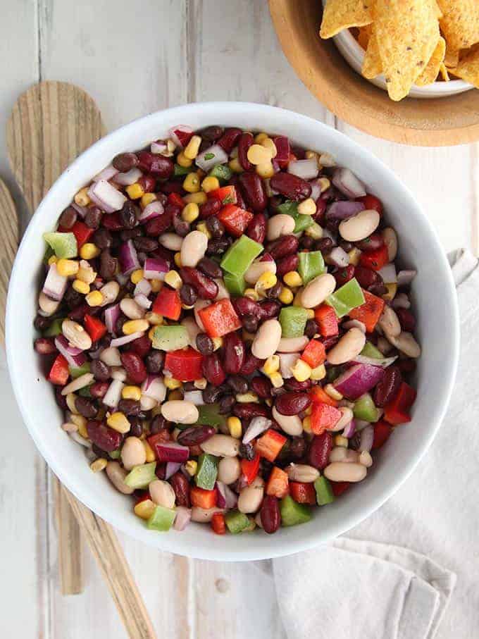 A white bowl of mexican bean salad on a white table
