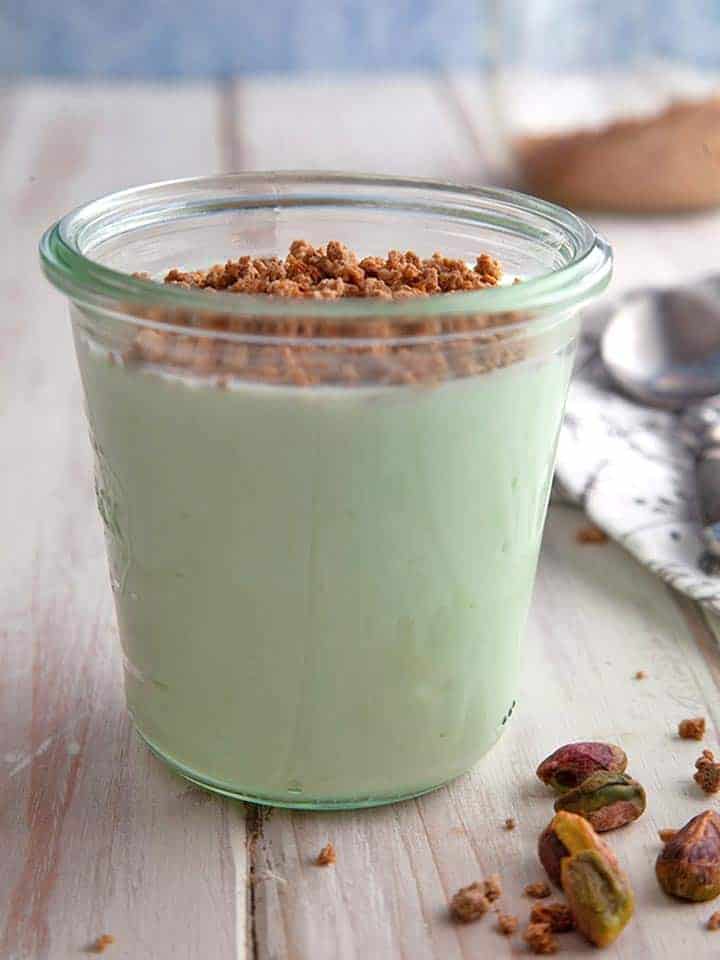 A jar of green pistachio crunch dessert on a white table
