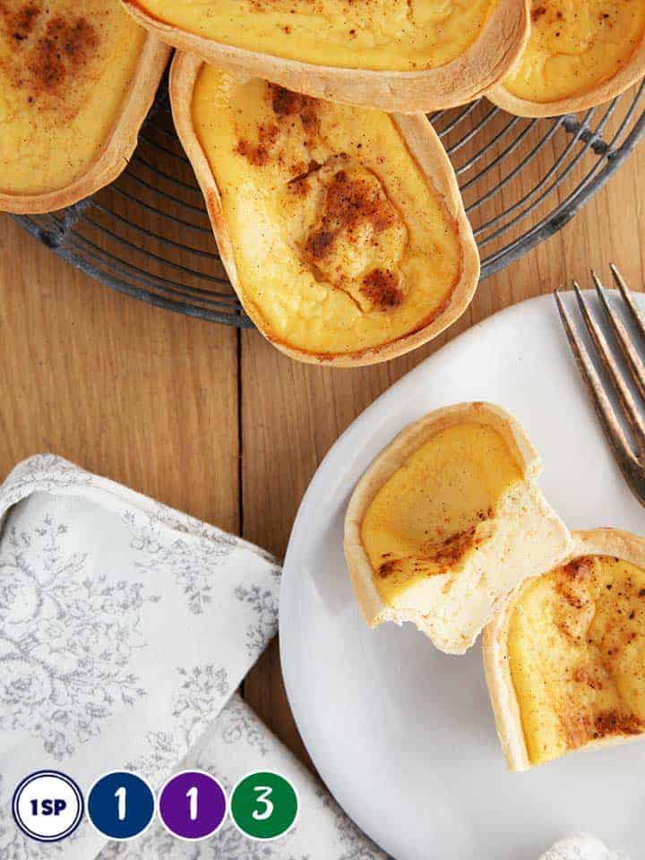 A wooden table with 5 custard tarts on a wire rack