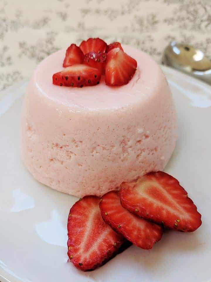 A pink fluff dessert on a white plate surrounded by strawberries