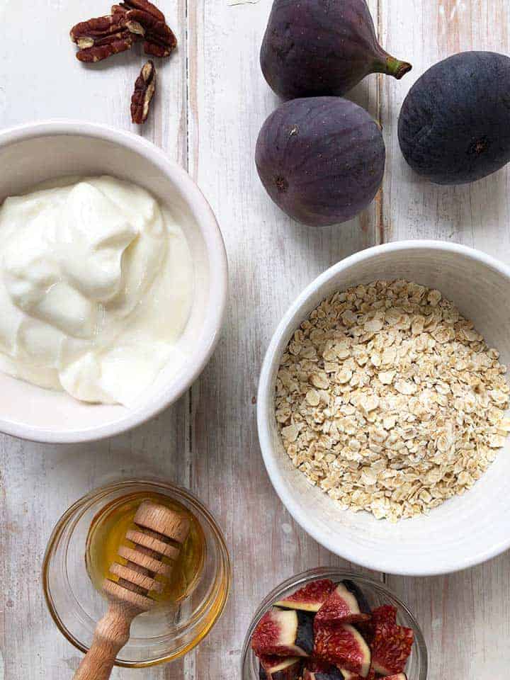 White bowls full of yogurt and oats, some figs, pecans and honey