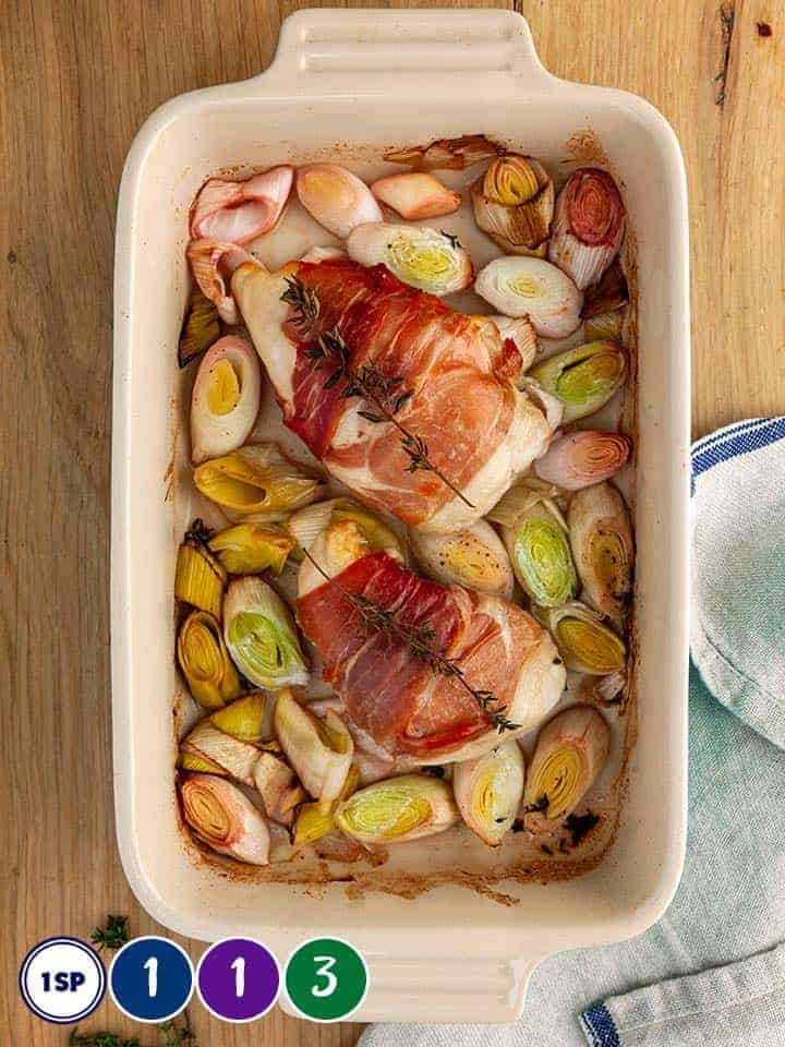 A dish of leeks and chicken on a wooden table