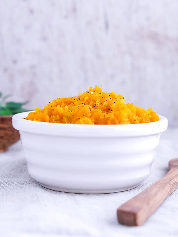 A white dish on a white table full of squash mash