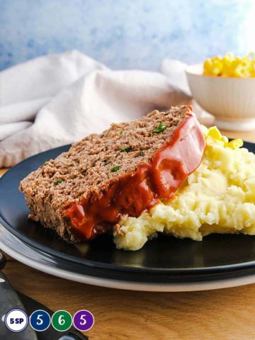 A black plate with a slice of meatloaf on mashed potato.