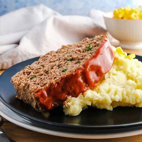 A black plate with a slice of meatloaf on mashed potato.