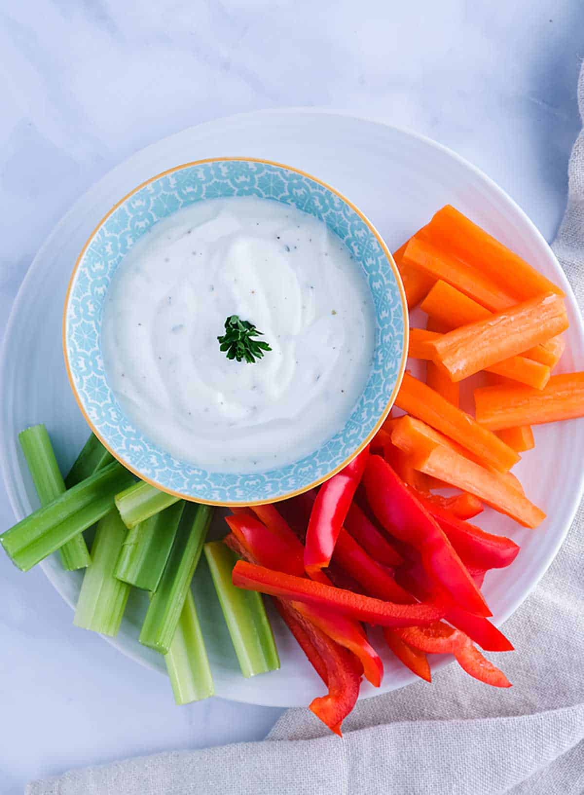 A bowl of ranch dip with carrots, celery and red pepper