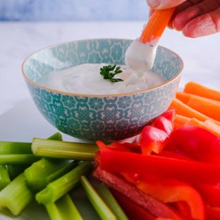 A carrot stick being dipped into a bowl of ranch dip