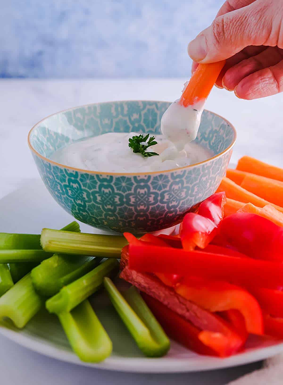 A carrot stick being dipped into a bowl of ranch dip
