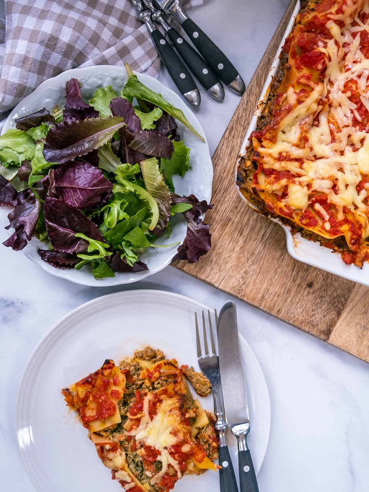 A white table with a bowl of salad and a dish of lasagna