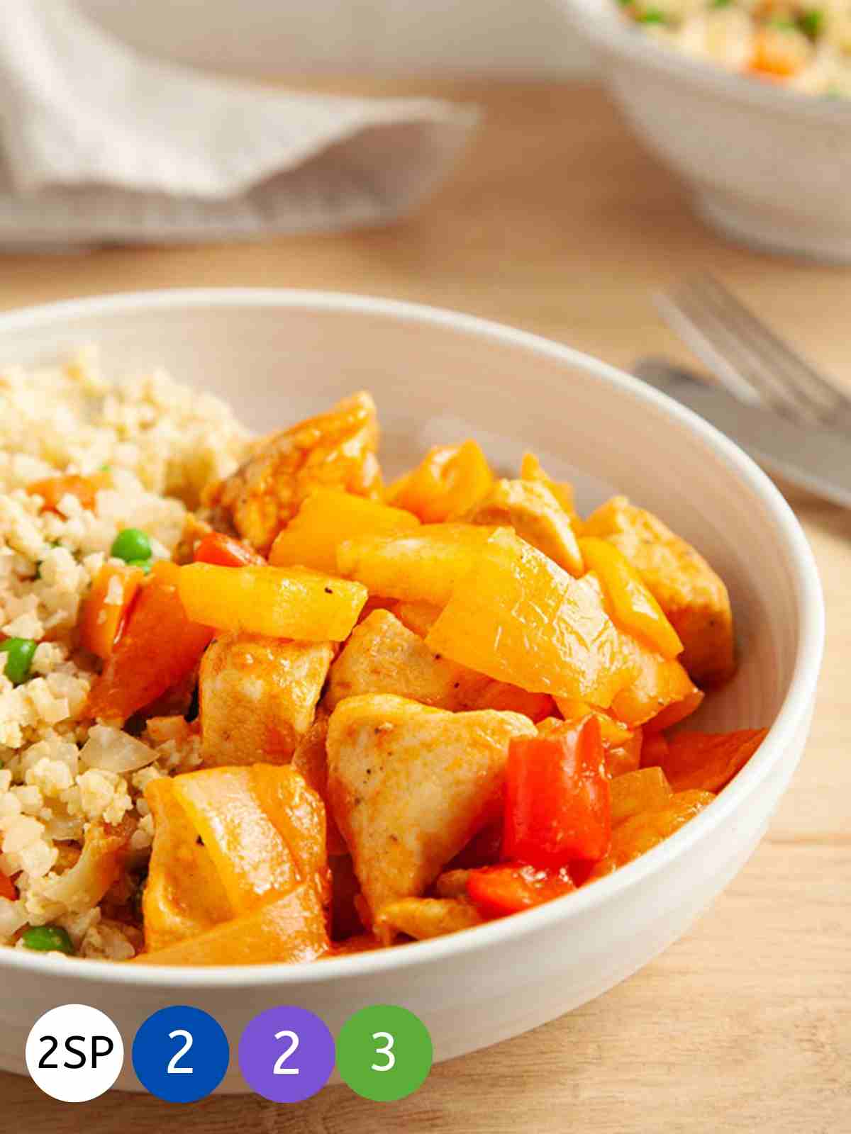 A white bowl full of sweet & sour chicken and some cauliflower rice. 