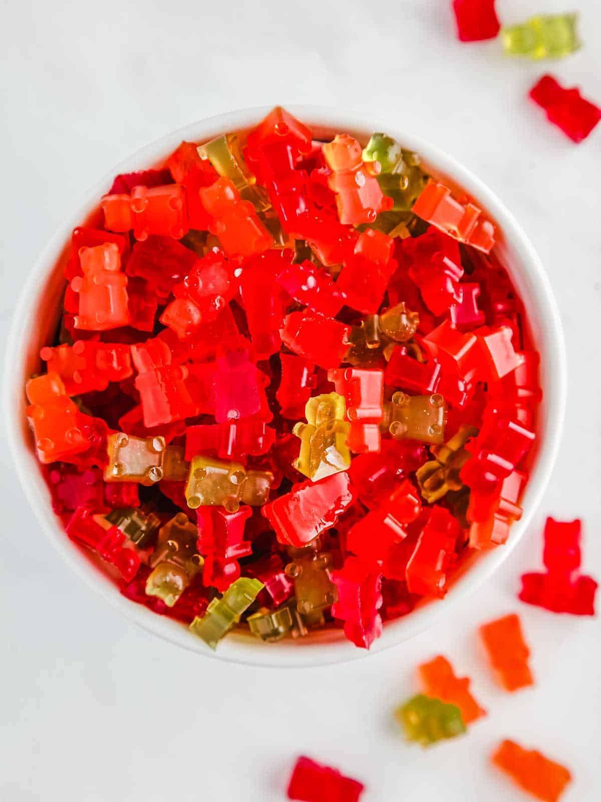 A white bowl of red, green and orange gummy bears on a white table