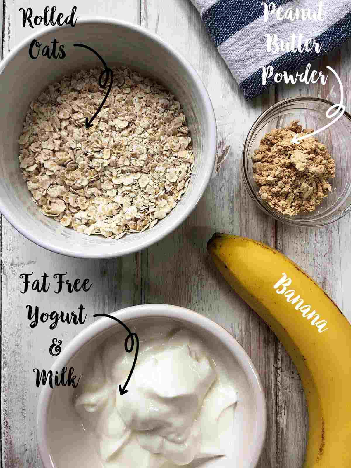 Bowls filled with yogurt, rolled oats and PB powder and a banana on a white table