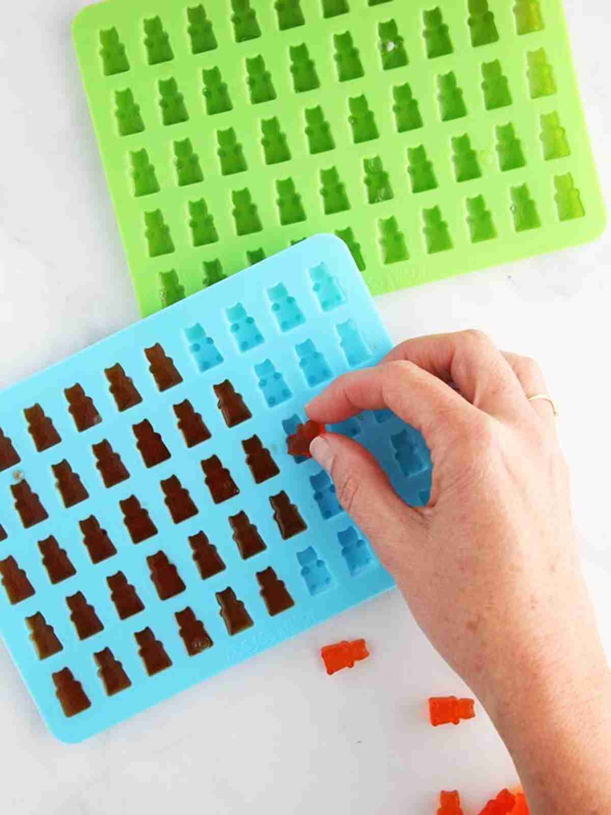 A hand removing gummy bears from a silicone mold