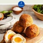 Four scotch eggs on a wooden board with one egg cut in half