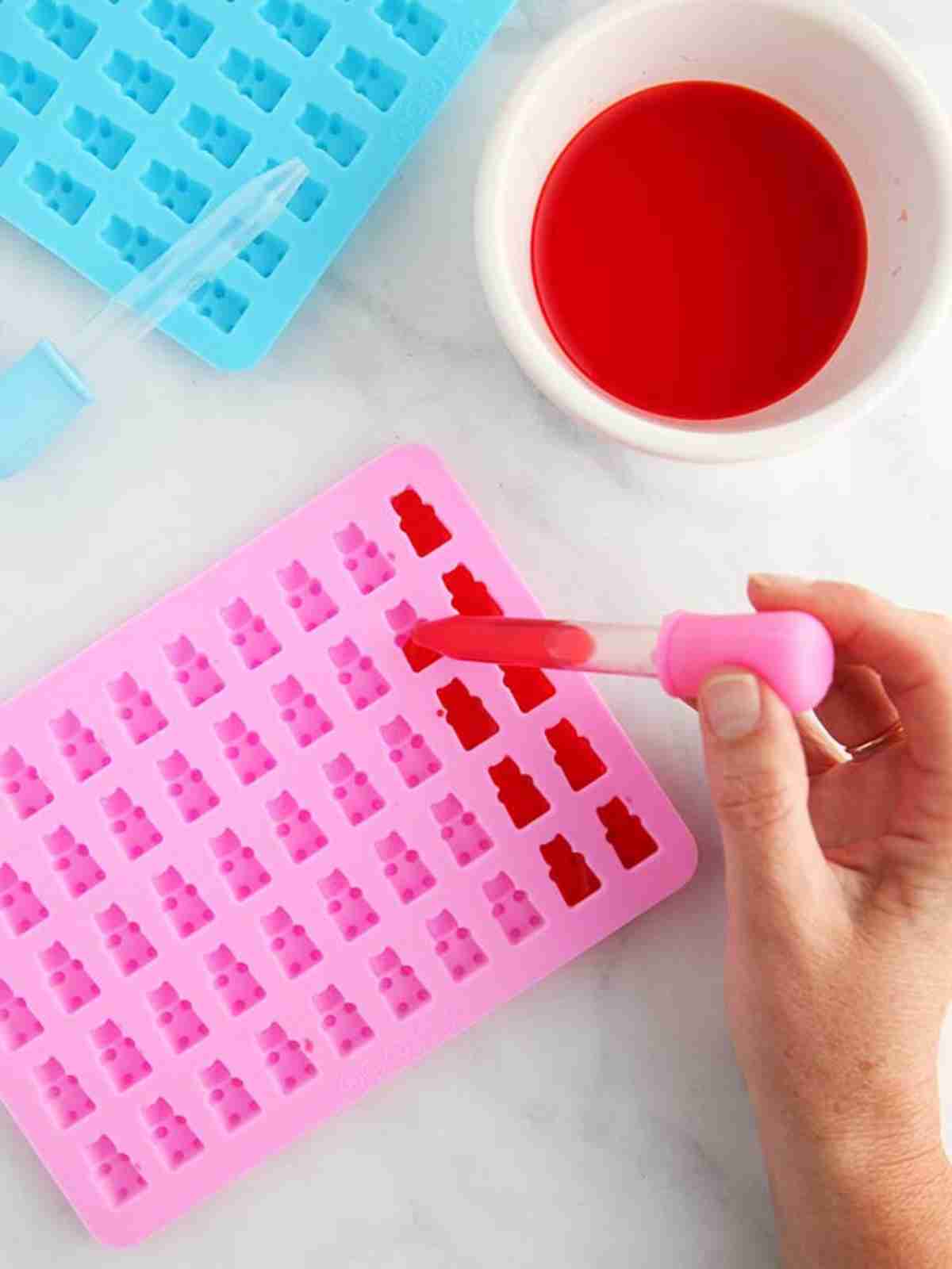 Using a pipette to add gummy bear mixture into a pink silicone mould