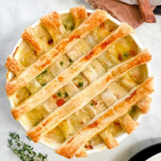 A dish of chicken pot pie with a pastry latticed top and a sprig of thyme