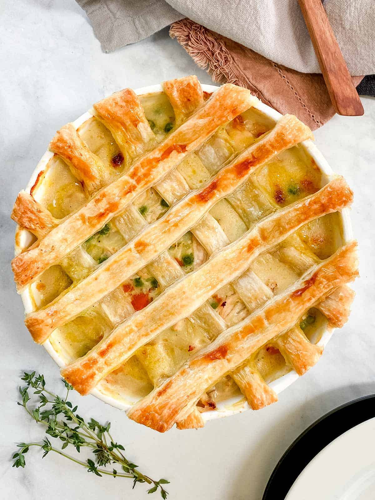 A dish of chicken pot pie with a pastry latticed top and a sprig of thyme