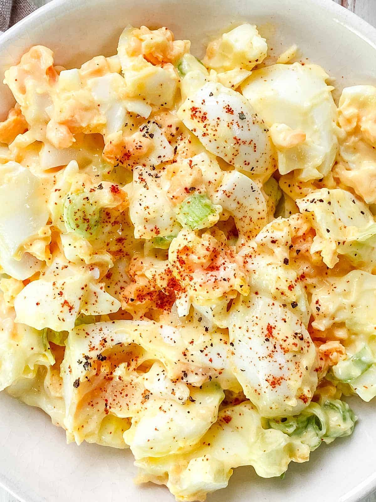 A close up of egg salad in a white bowl sprinkled with pepper and paprika