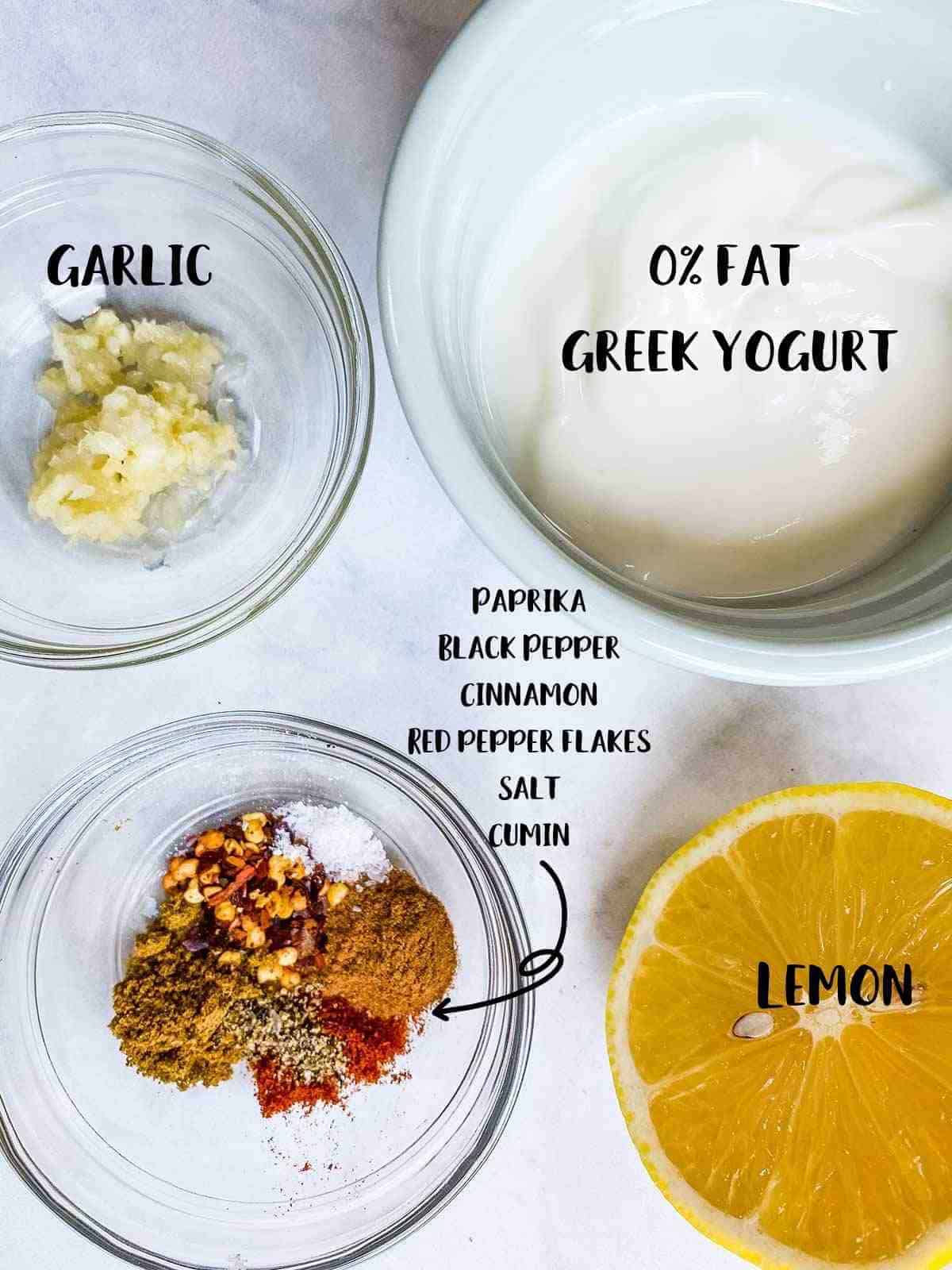 Small bowls of garlic, yogurt, and middle eastern spices and a lemon on a white table