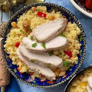 Sliced chicken on a bed of cous cous in a blue patterned bowl.