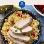 A decorative blue bowl full of couscous salad with sliced chicken on top