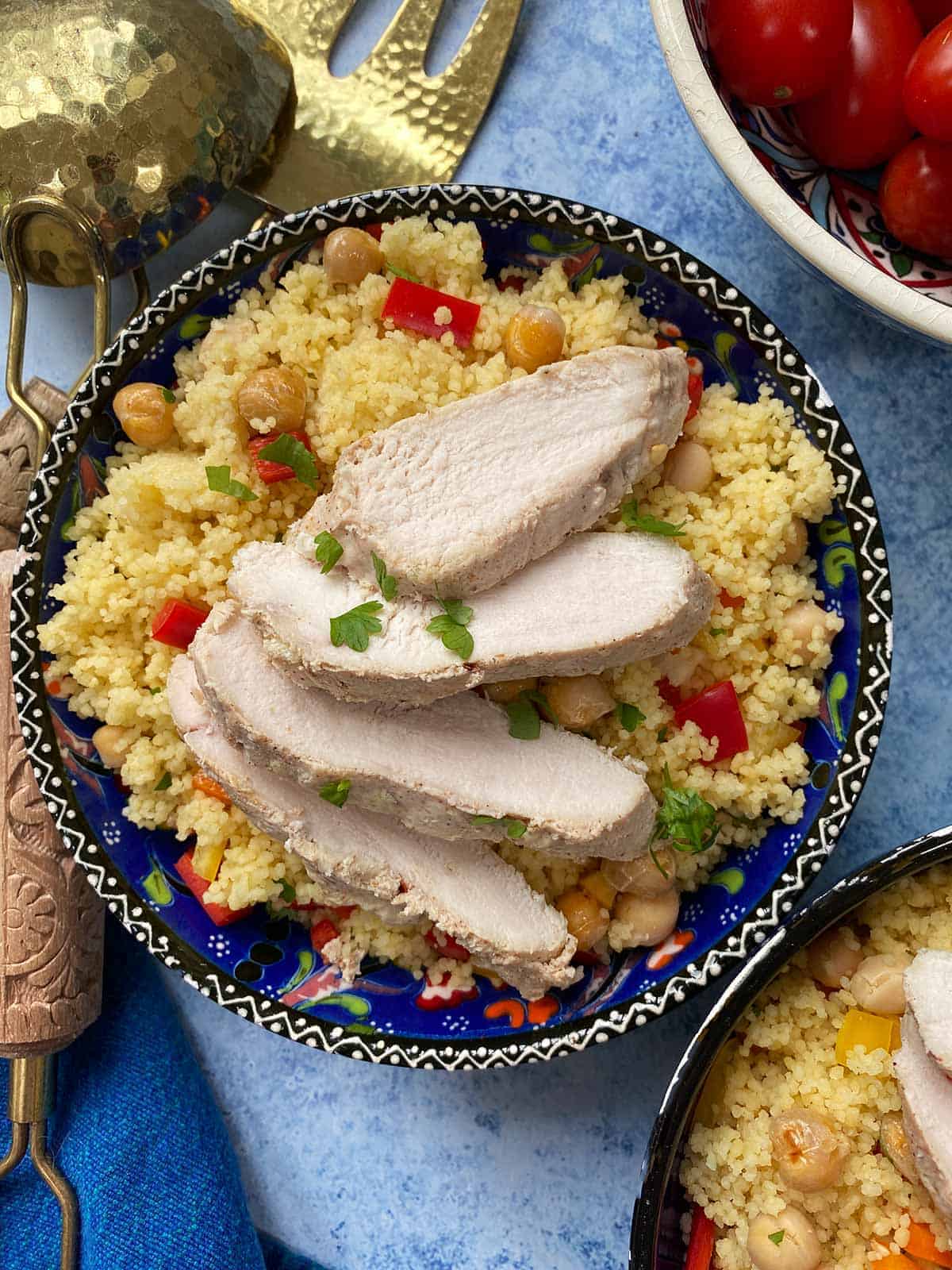 Sliced chicken on a bed of cous cous in a blue patterned bowl.