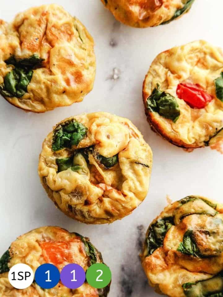 6 egg muffins with spinach and tomato on a marble table.