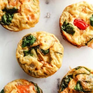 A white marble table with 6 tomato and spinach egg muffins.
