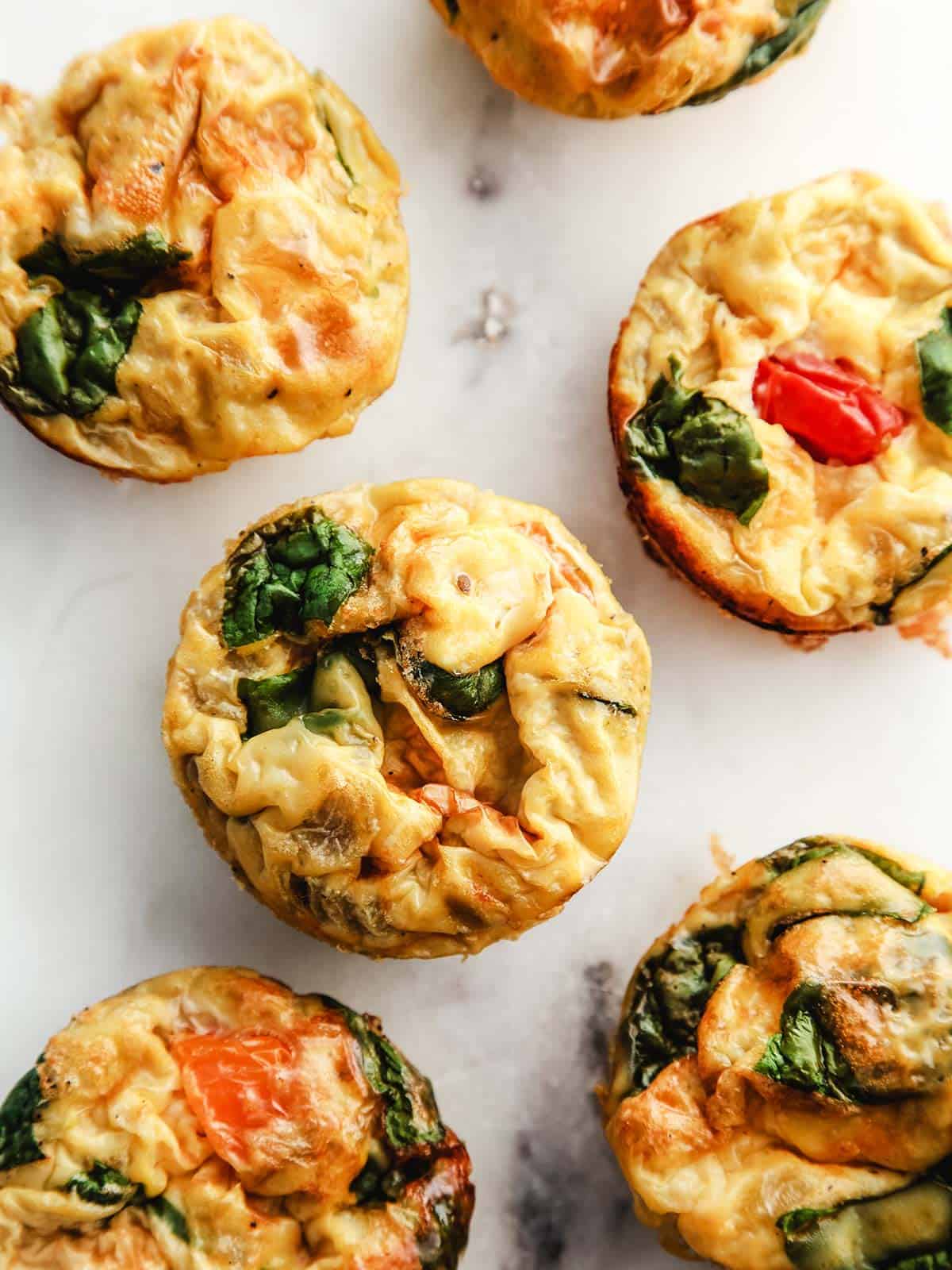 A white marble table with 6 tomato and spinach egg muffins.