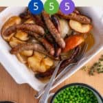 A white casserole dish full of sausages, onions and apples on a wooden table with a dish of garden peas and a dish of potatoes with text title overlay and smartpoint values.