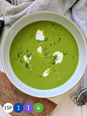 A white bowl full of green pea soup topped with a swirl of white yogurt.