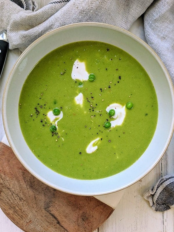 A bowl of pea soup with a drizzle of white yogurt on top.
