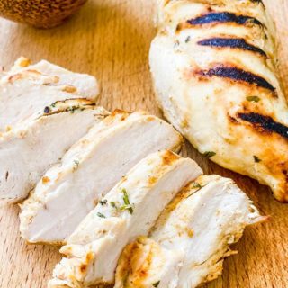 2 chicken breasts with grill marks, one sliced one whole on a wooden table.