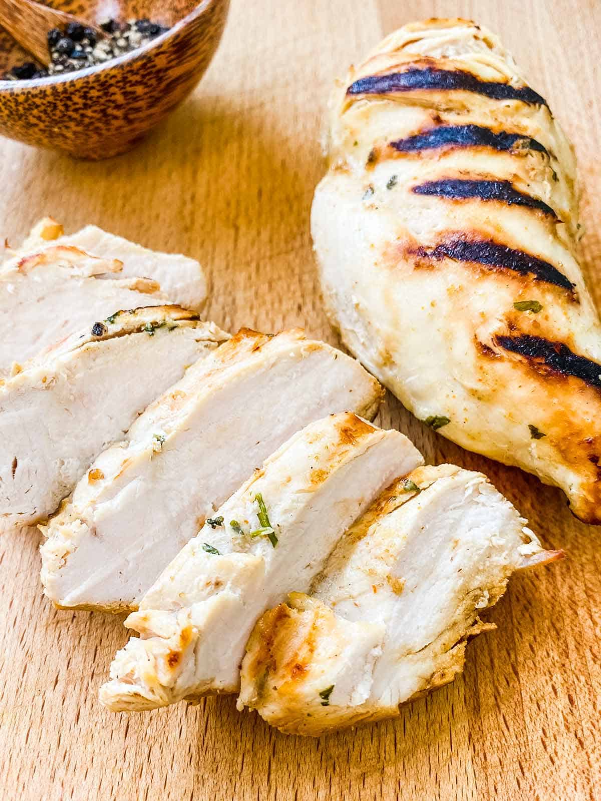 2 chicken breasts with grill marks, one sliced one whole on a wooden table.