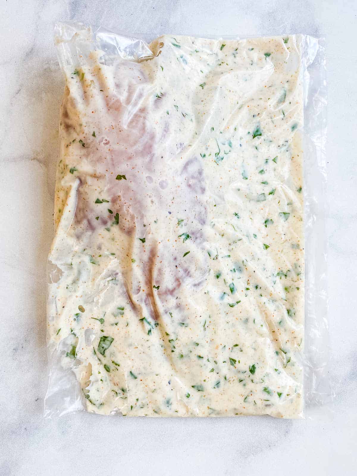 Chicken breast and marinade in a baggie on a white marble table.