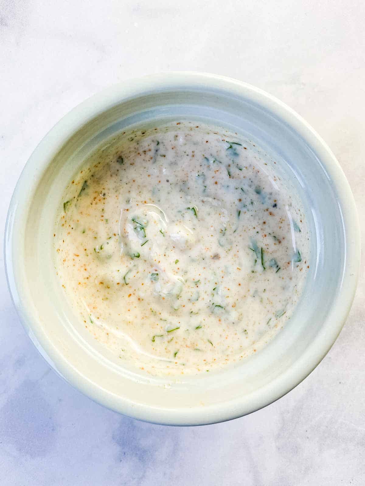 A white dish of yogurt marinade on a marble table.