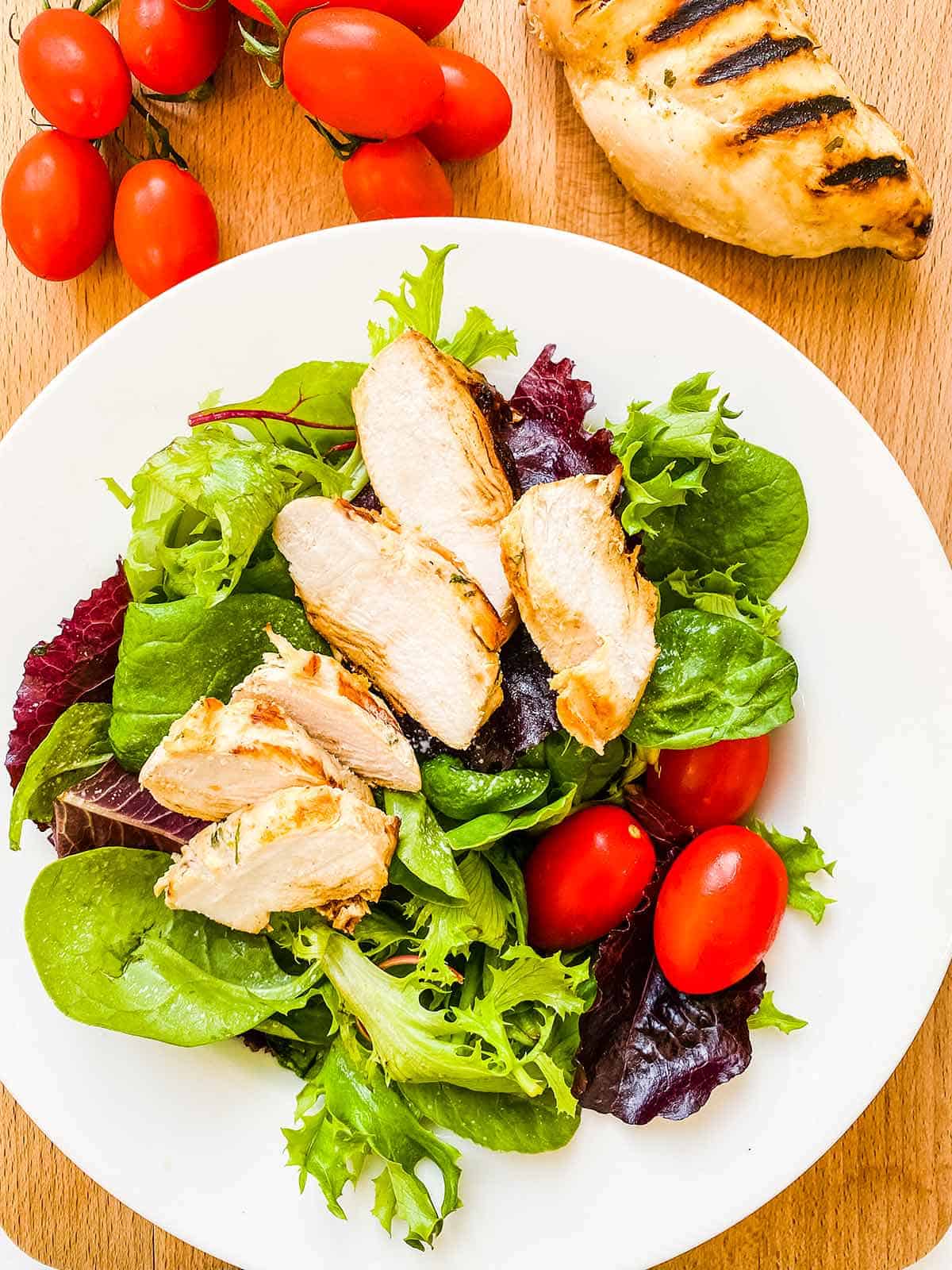 A white bowl full of lettuce and tomatoes with sliced chicken on top.