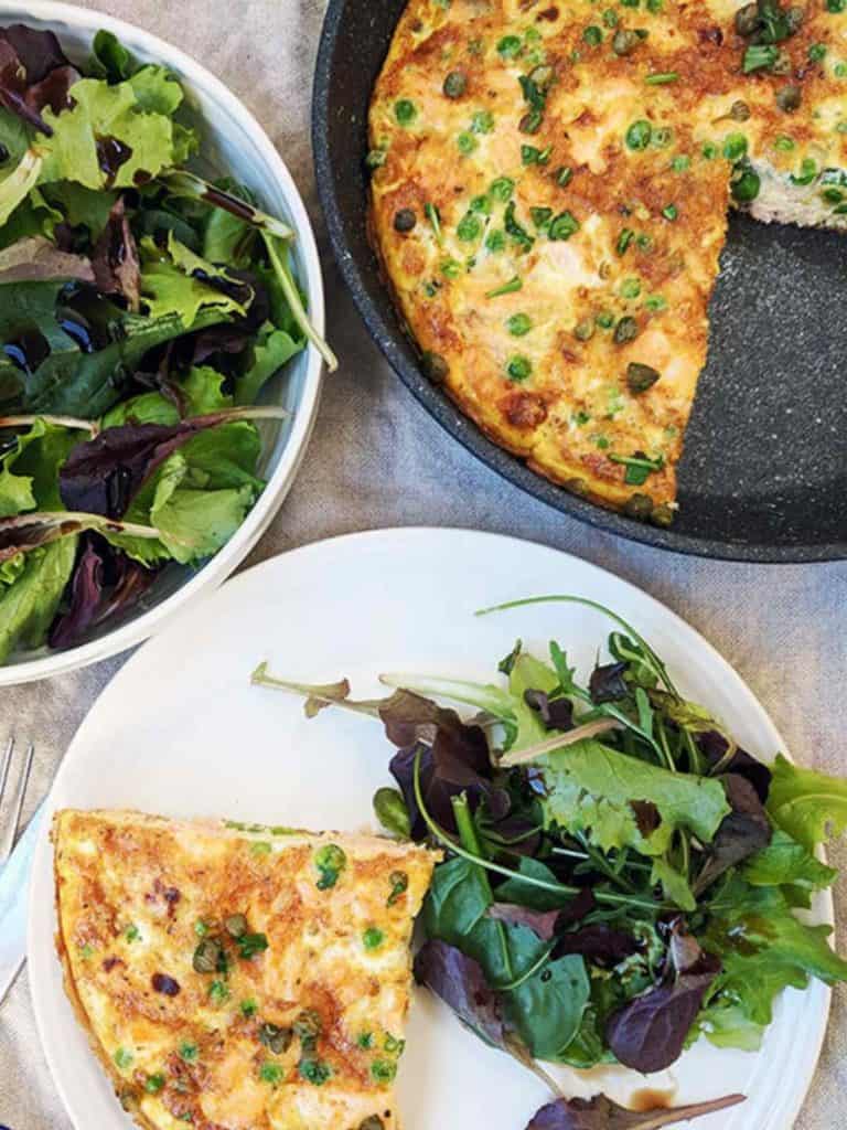 A skillet and plate of salmon & pea frittata with a side salad.