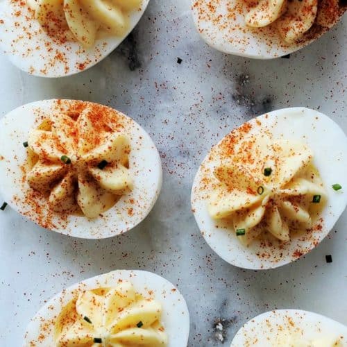 A marble table with 6 deviled eggs dusted with paprika and chives.