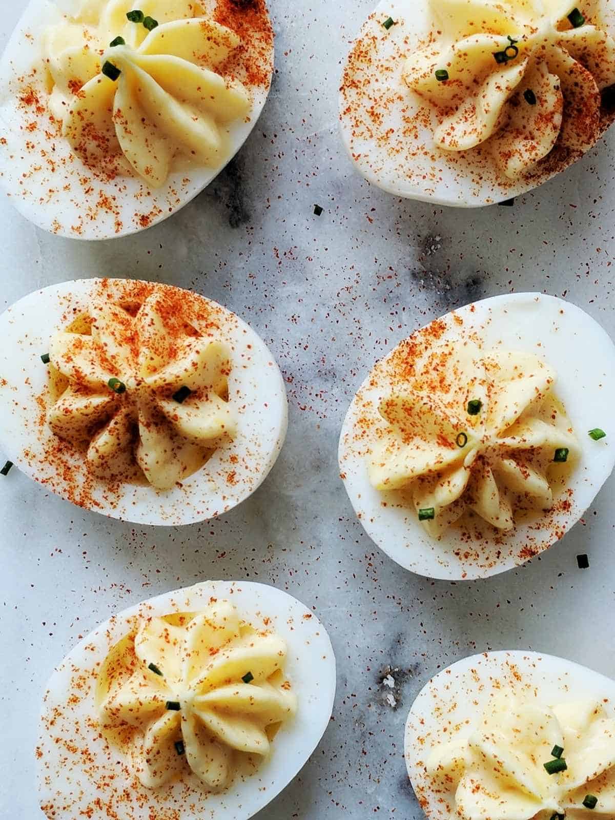 A marble table with 6 deviled eggs dusted with paprika and chives.