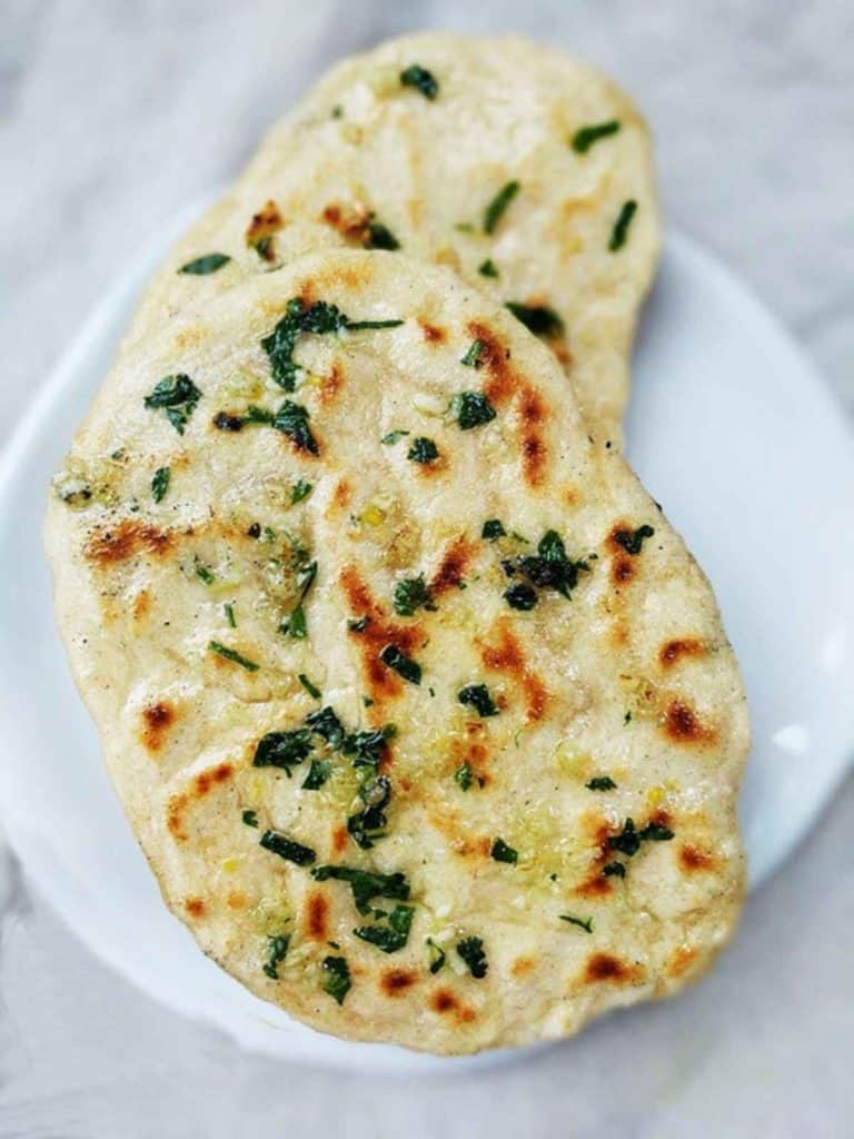 2 garlic naan breads on a white plate on a white marble table.