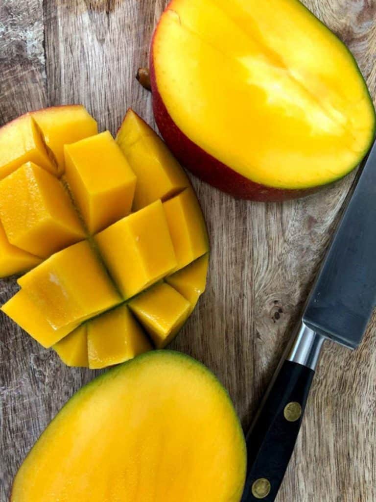A cubed mango on a wooden board with a knife.
