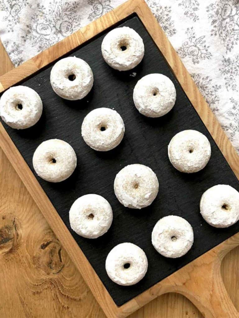 A tray of mini doughnuts dusted with sugar on a wooden table.